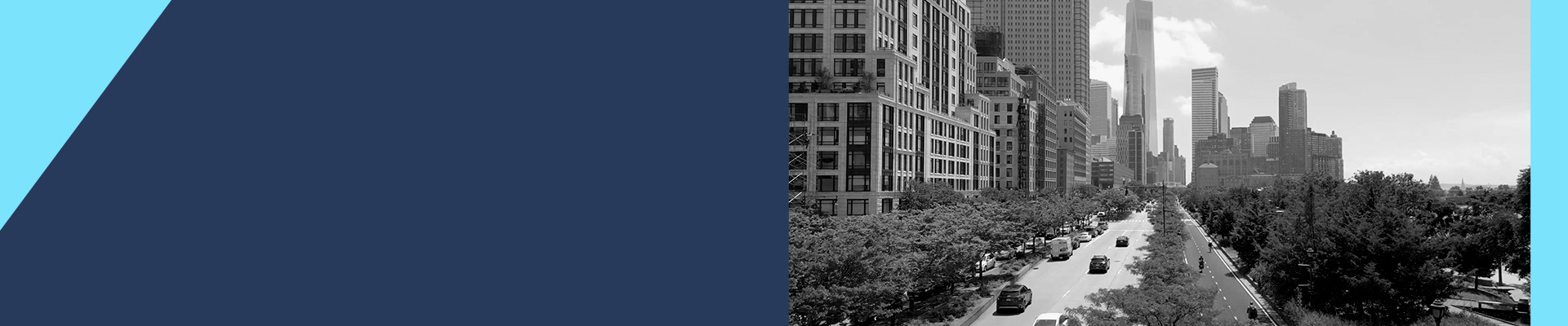 Wide angle view of a tree-lined avenue in New York City, with traffic moving toward One World Trade Center and the Lower Manhattan skyline in the background.