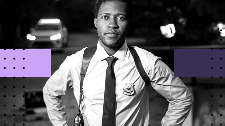 A police officer standing near a roadway with a car in the background.